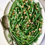 Green Bean Salad with Mustard Vinaigrette on white oval platter garnished with walnuts.