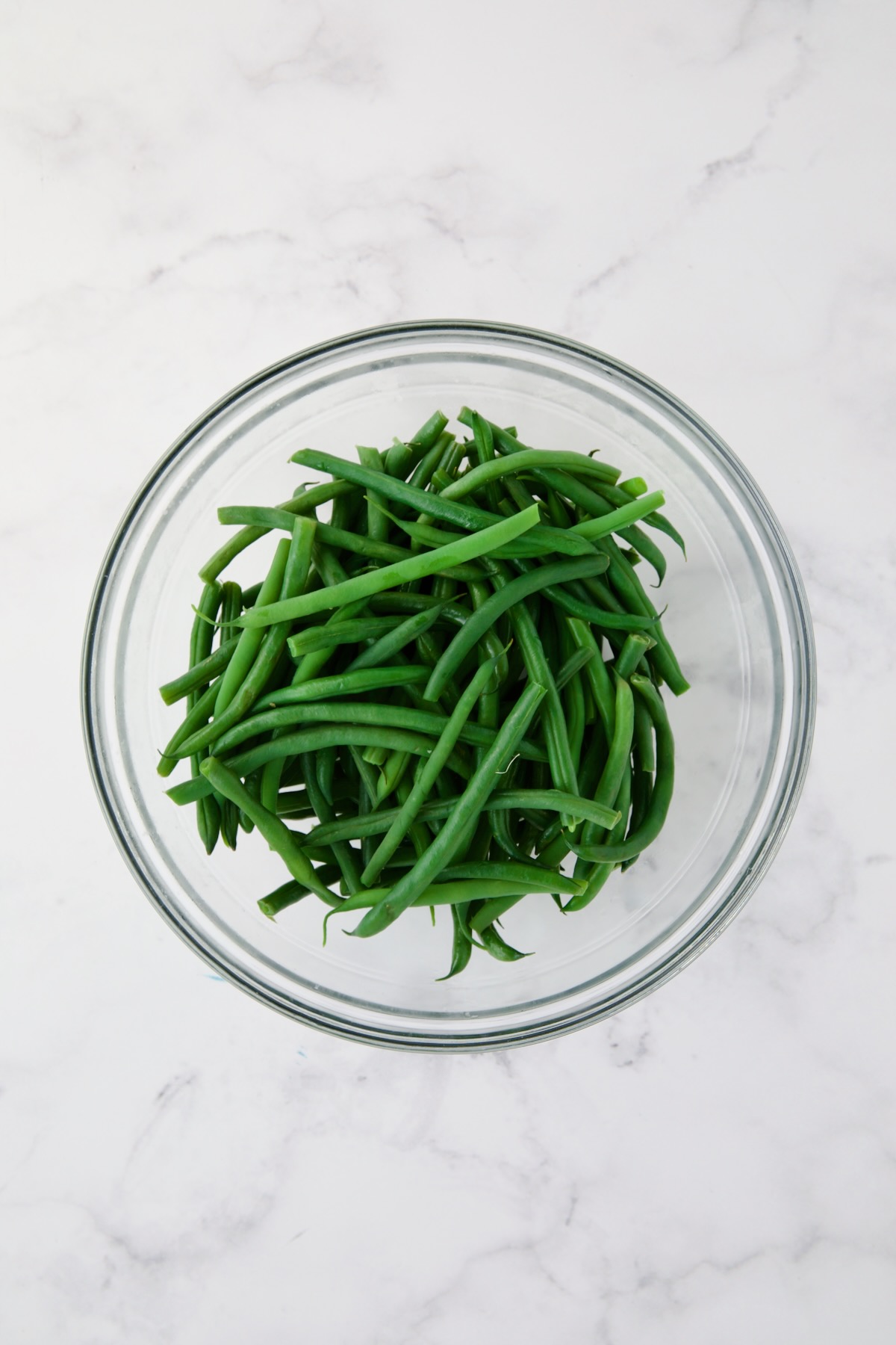 Steamed green beans in glass bowl.