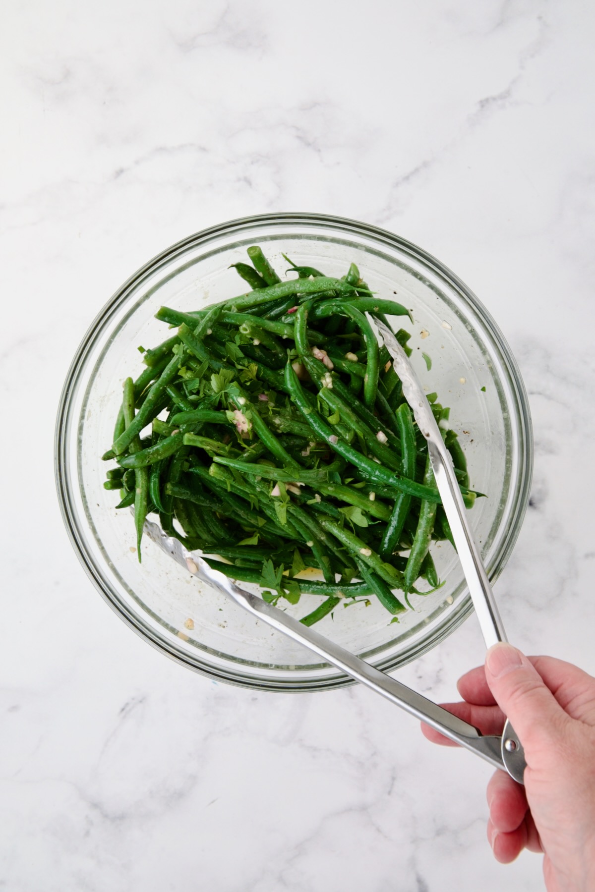Green beans being tossed with vinaigrette in glass bowl.