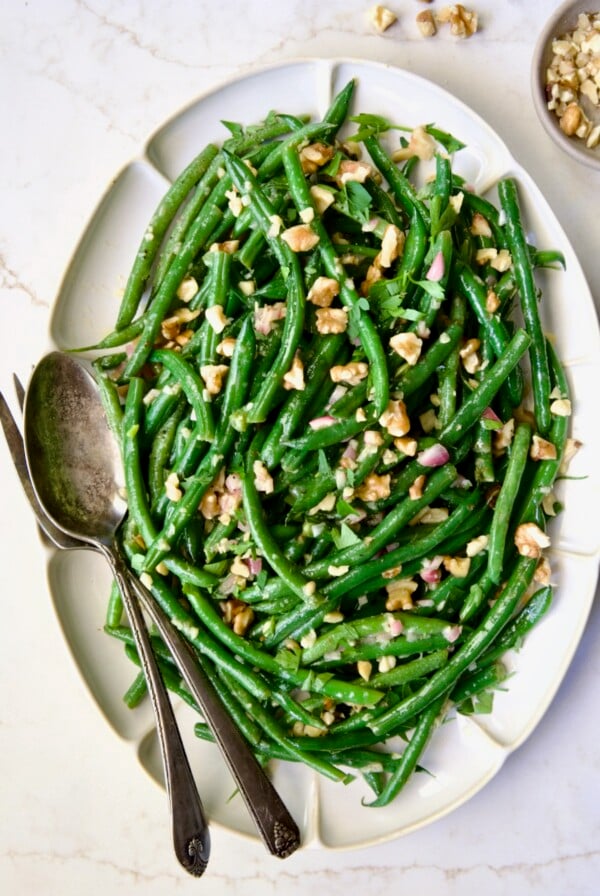 Green Bean Salad with Mustard Vinaigrette on white oval platter garnished with walnuts.