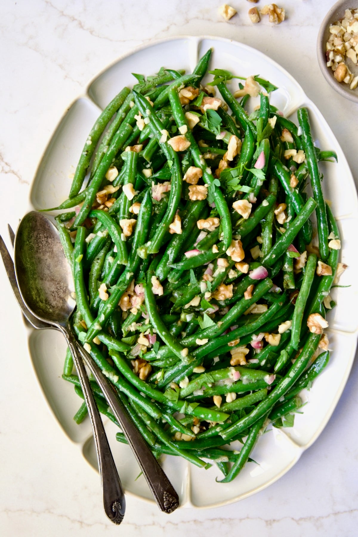 Green Bean Salad with Mustard Vinaigrette on white oval platter garnished with walnuts.