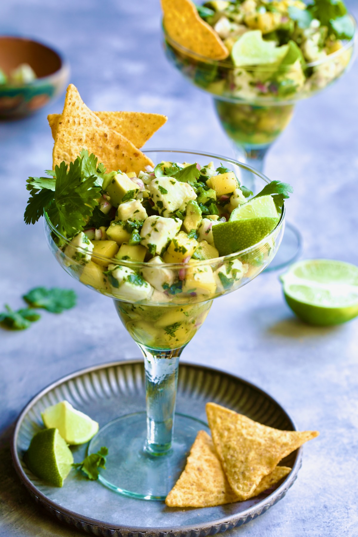 Halibut Ceviche with mango, avocado, lime wedges, cilantro sprigs and tortilla chips in margarita glass.