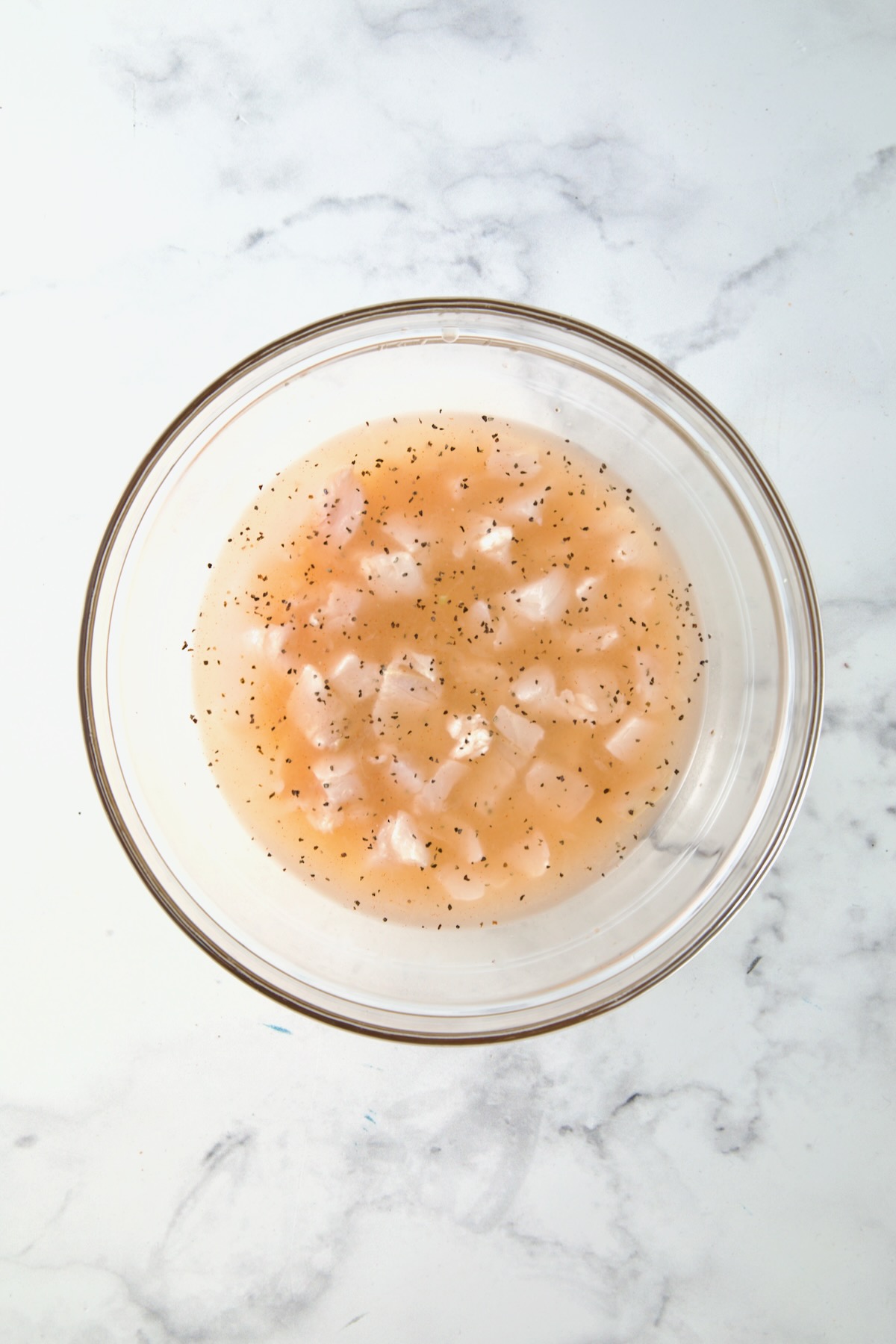 Halibut cubes immersed in marinade in glass bowl.