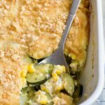 Zucchini Corn Casserole in white rectangular baking dish with serving spoon scooping some out.