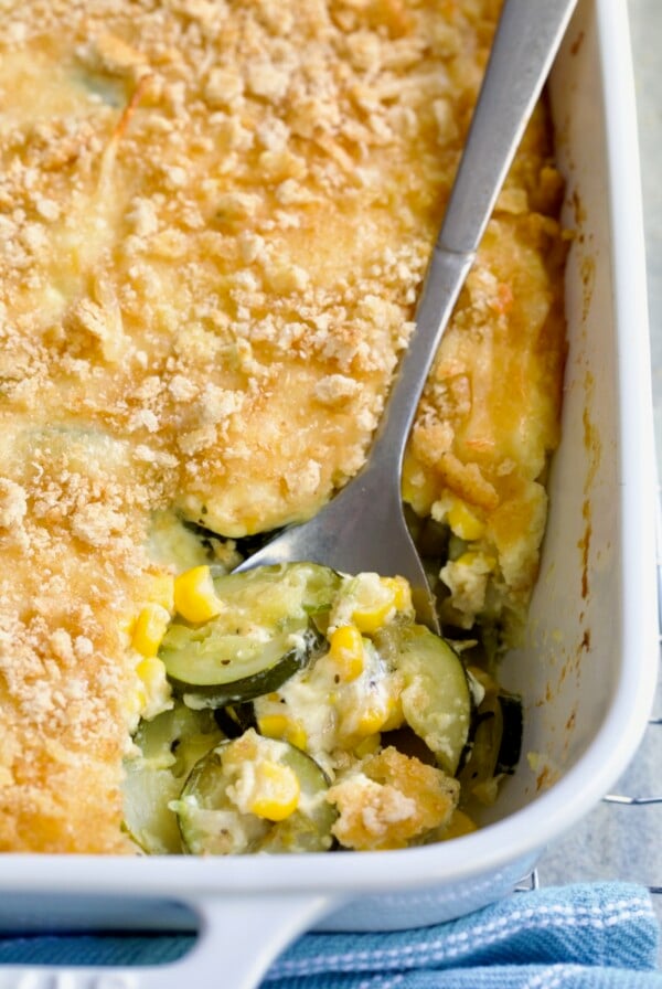 Zucchini Corn Casserole in white rectangular baking dish with serving spoon scooping some out.