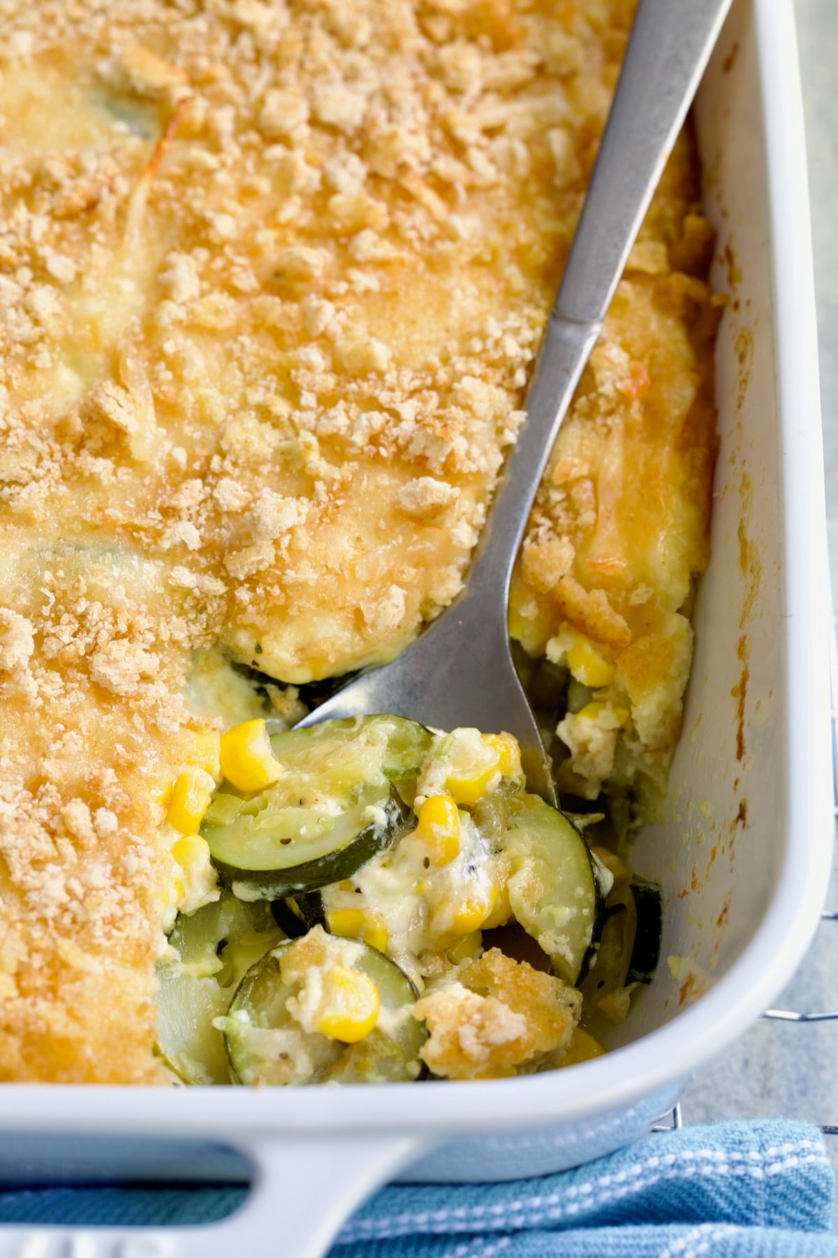 Zucchini Corn Casserole in white rectangular baking dish with serving spoon scooping some out.
