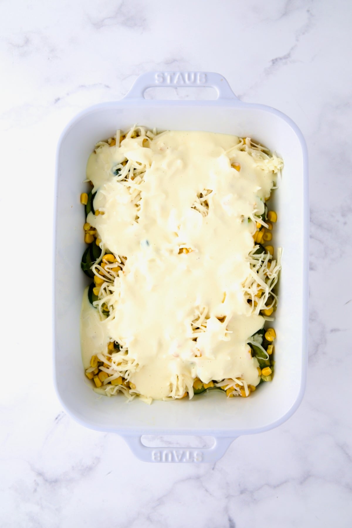 Egg combination poured over zucchini, corn and cheese in white rectangular baking dish.
