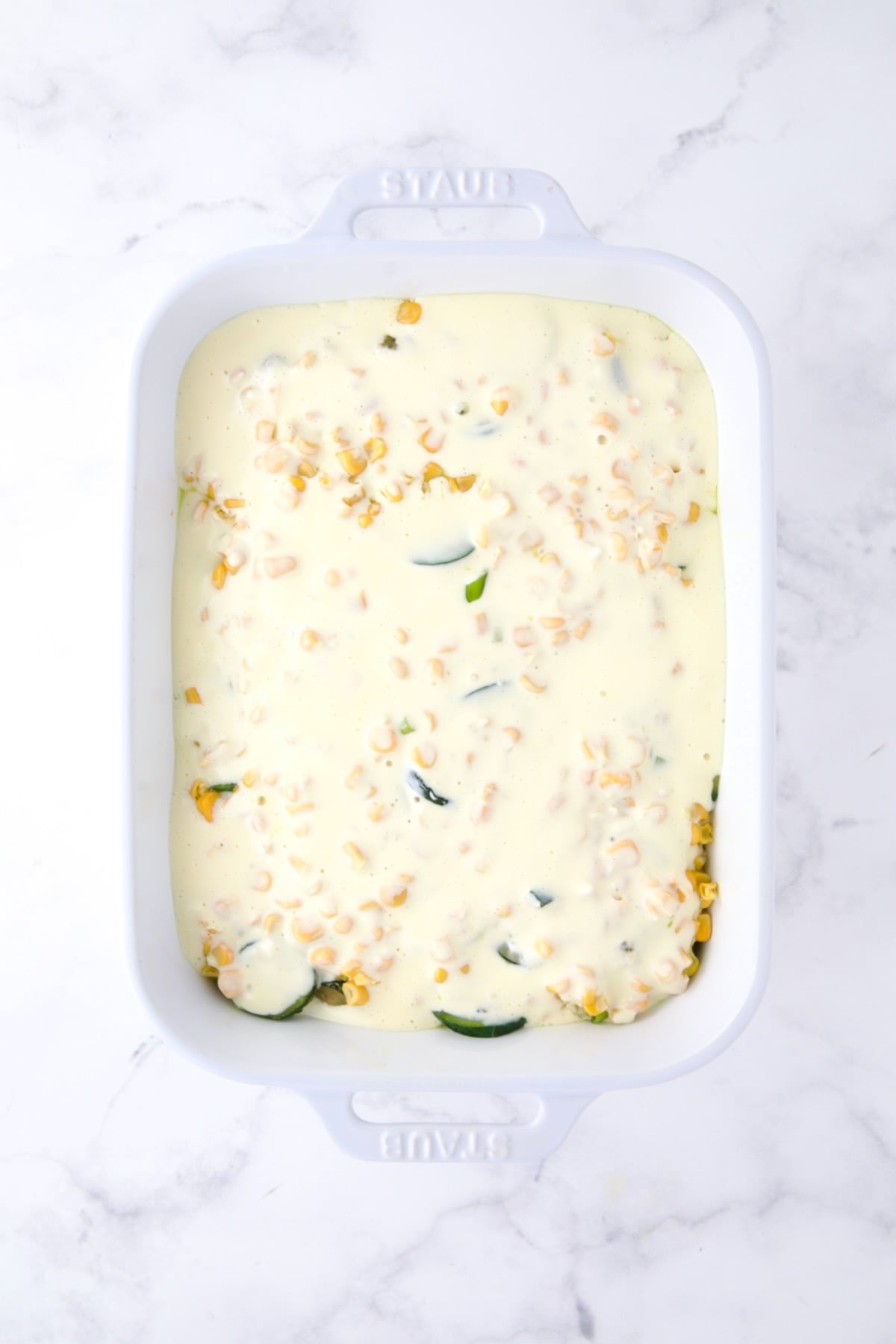 Final layer of egg mixture added to casserole in white rectangular baking dish.