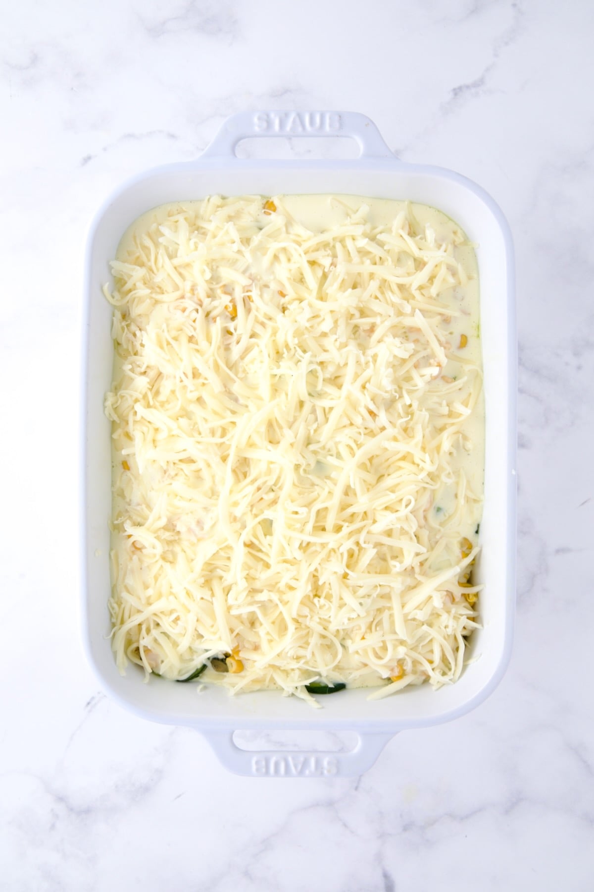 Final layer of cheese added to casserole in white rectangular baking dish.