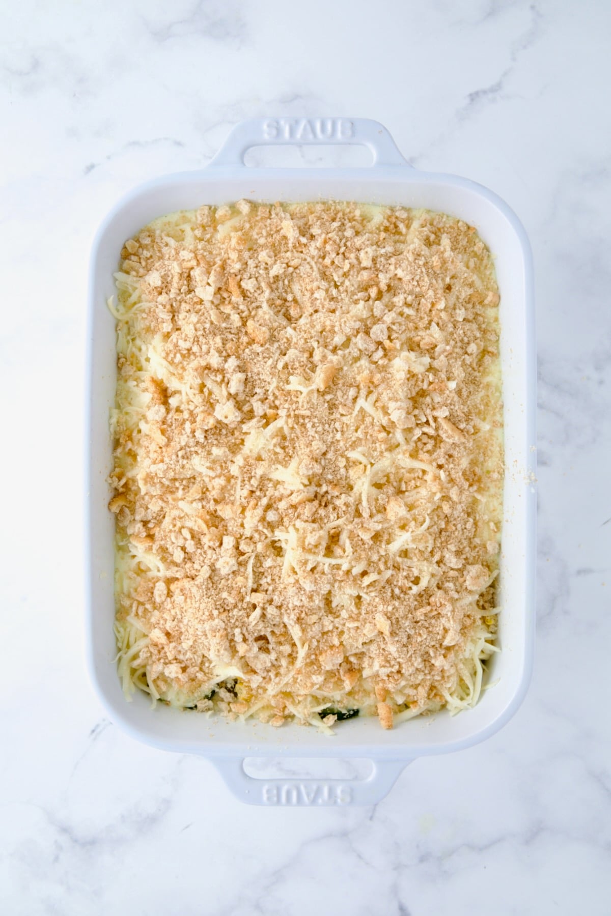 Crushed crackers added to casserole in white rectangular baking dish.