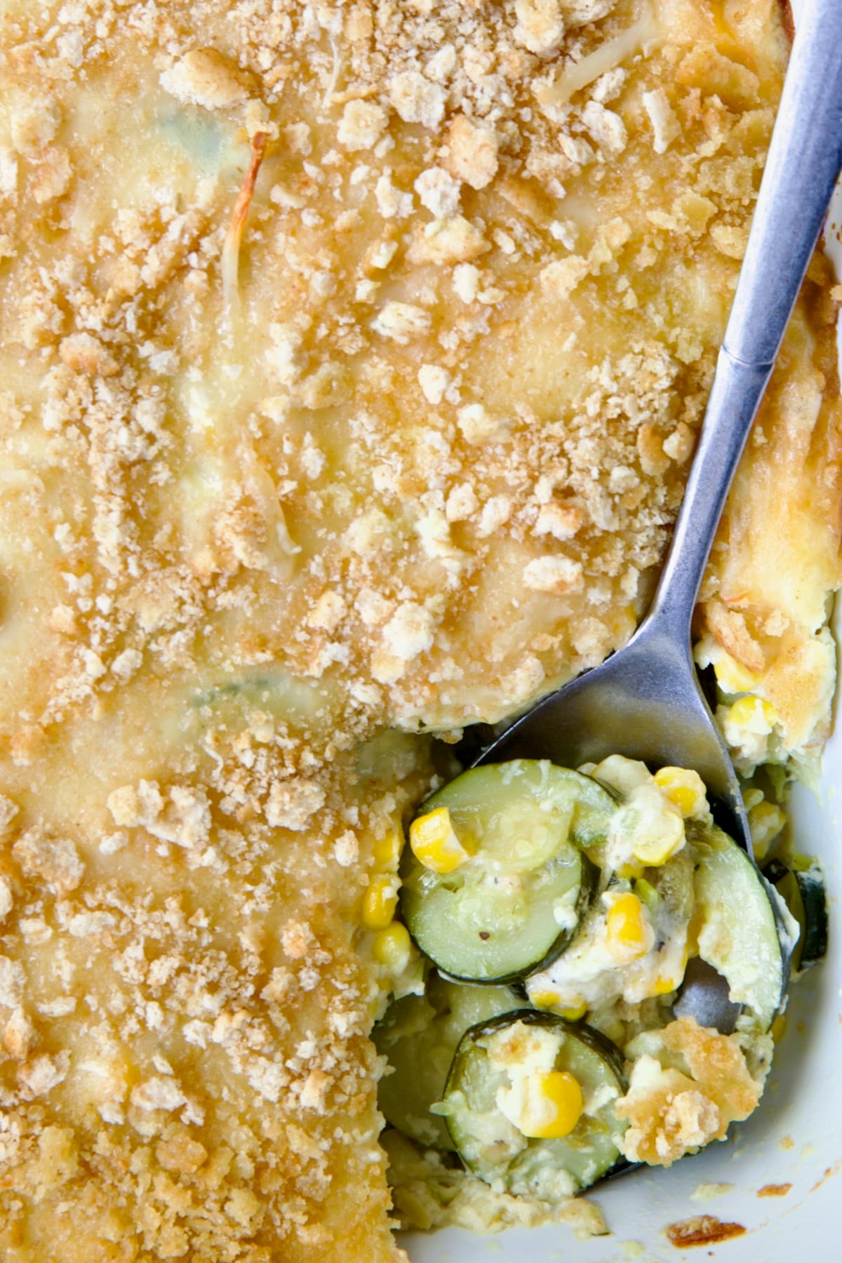 Zucchini Corn Casserole in white rectangular baking dish with serving spoon scooping some out.
