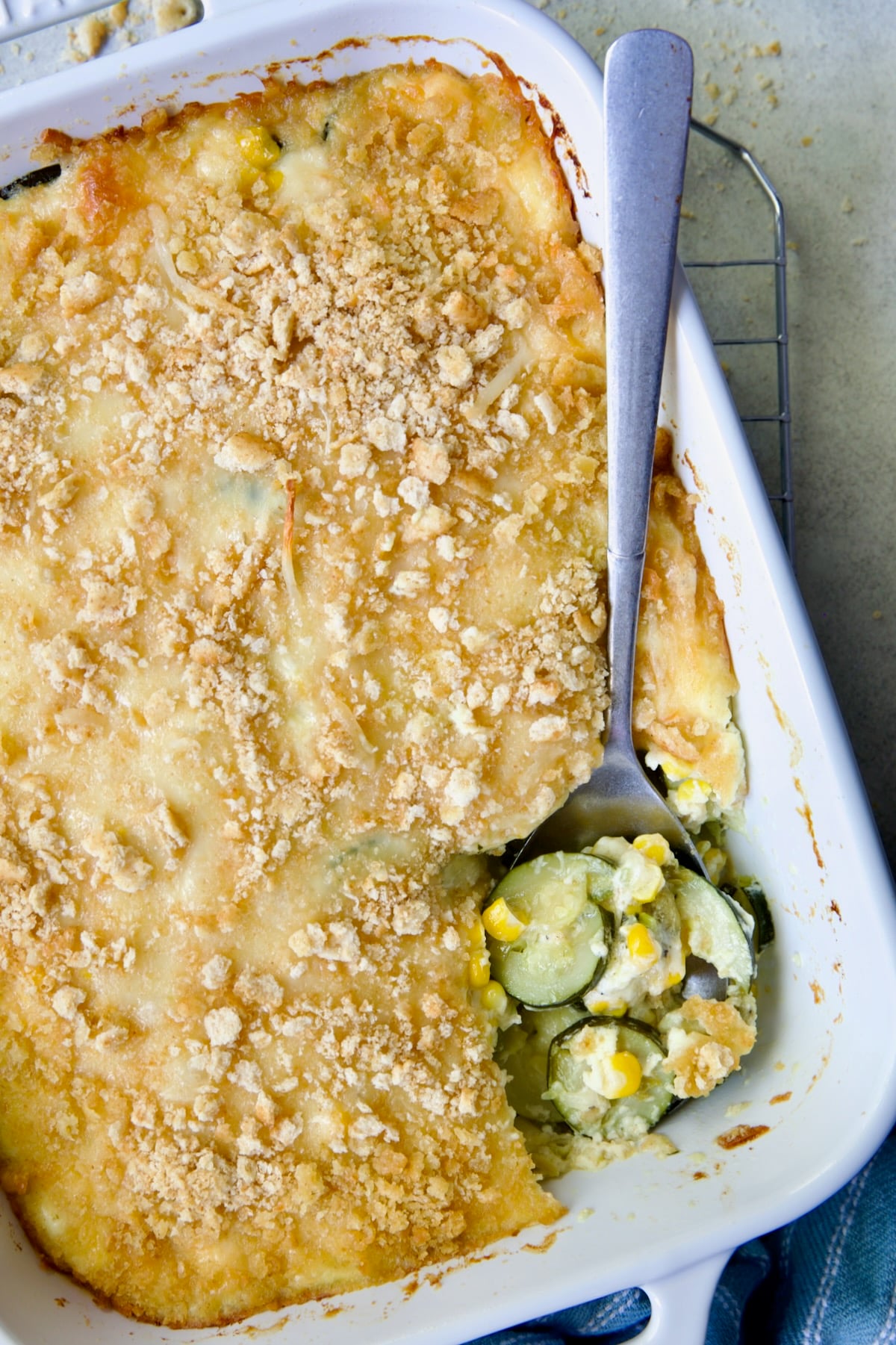 Zucchini Corn Casserole in white rectangular baking dish with serving spoon scooping some out.