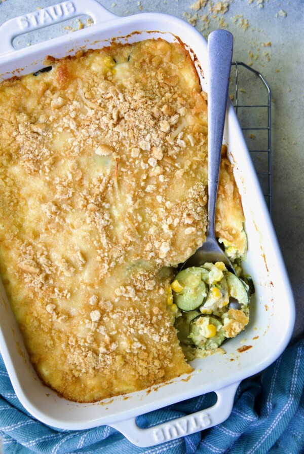 Zucchini Corn Casserole in white rectangular baking dish with serving spoon scooping some out.