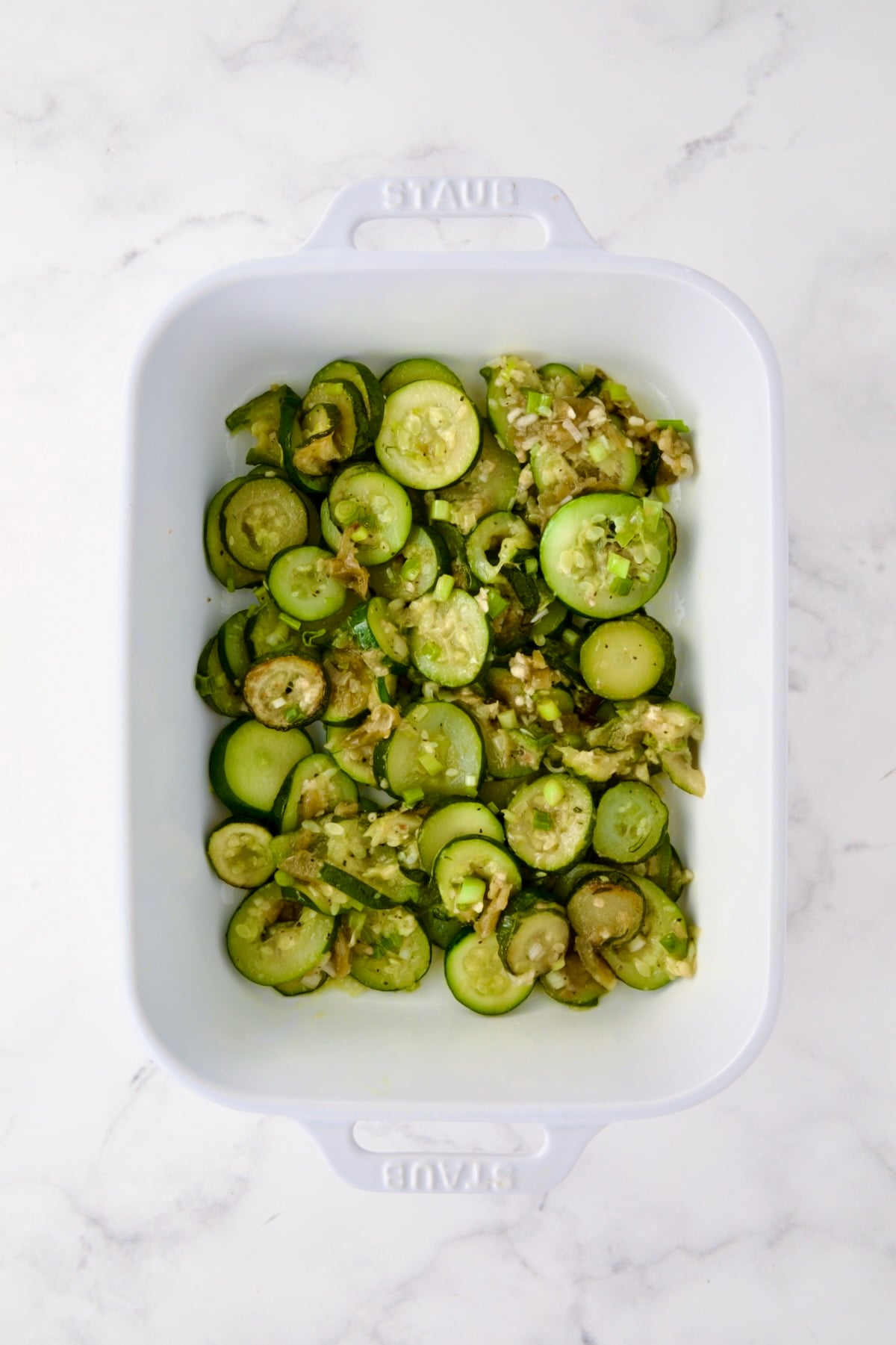 First layer of zucchini rounds, scallions and green chiles in white rectangular baking dish.