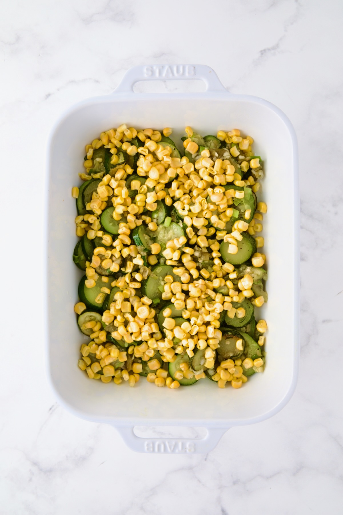 Corn added to zucchini in white rectangular baking dish.