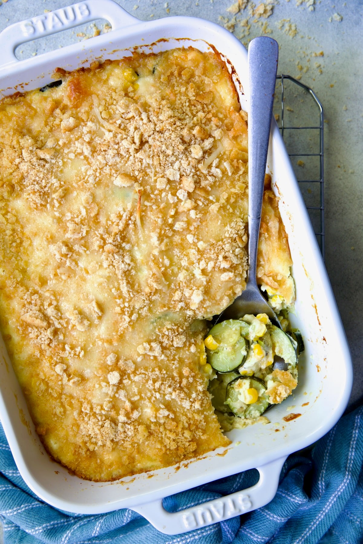 Zucchini Corn Casserole in white rectangular baking dish with serving spoon scooping some out.