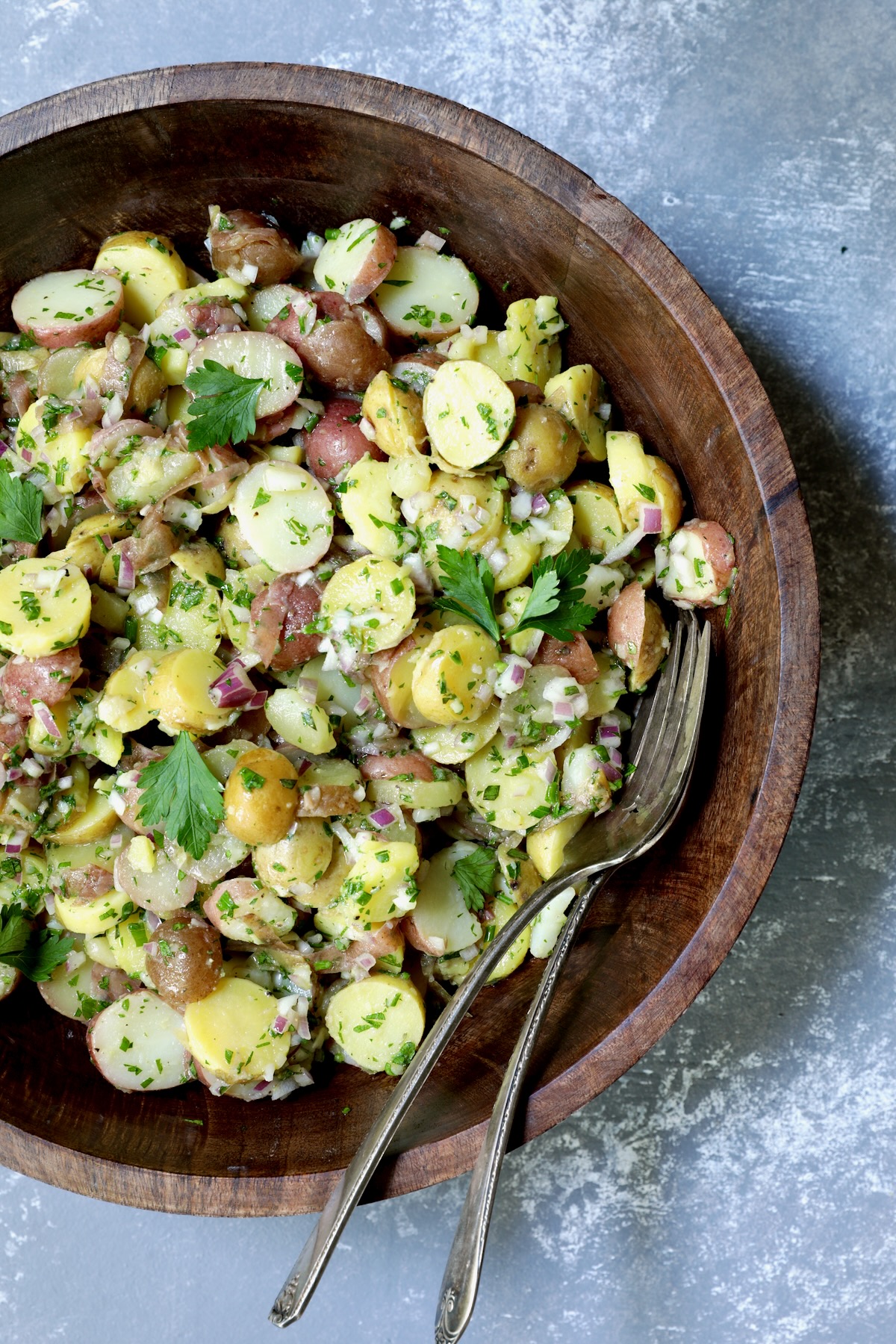 French Potato Salad in dark wood bowl with serving utensils.