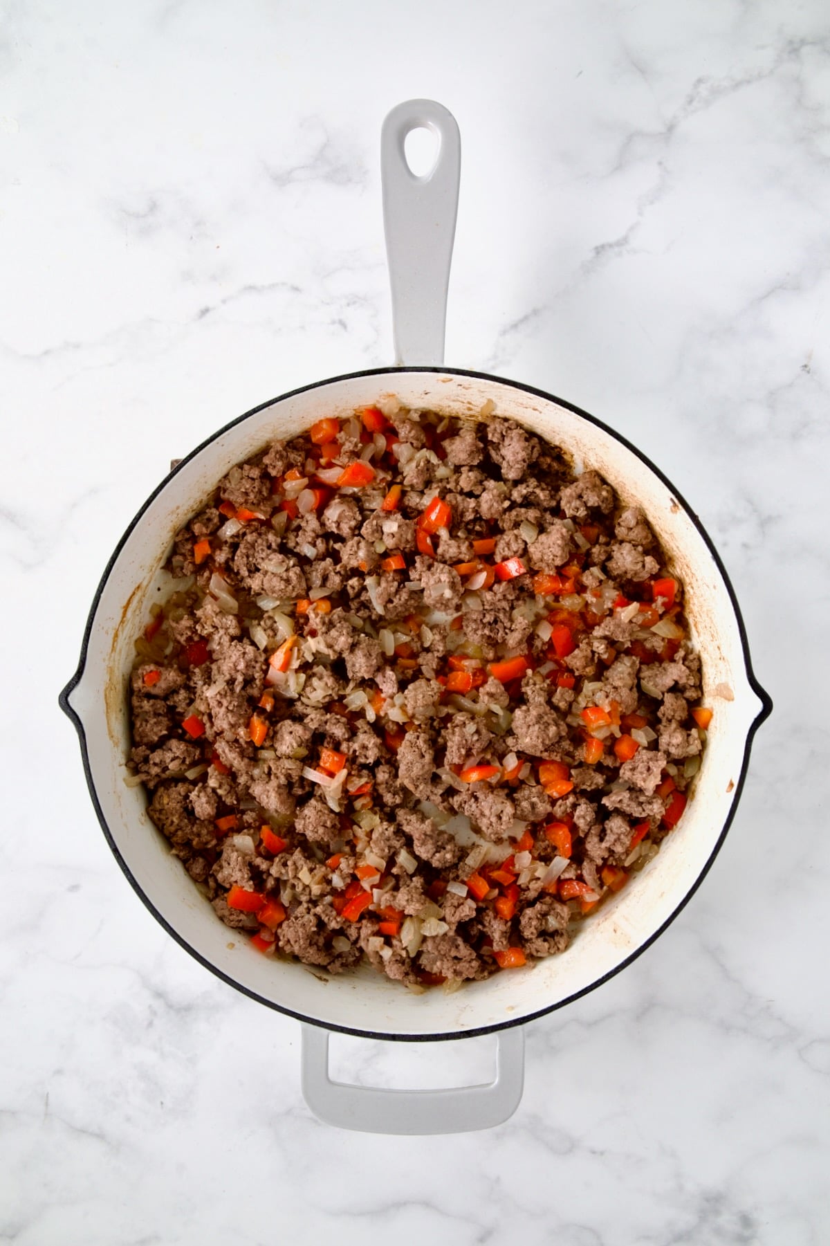 Cooked ground beef, red bell pepper and onions in white enamel cast iron skillet.