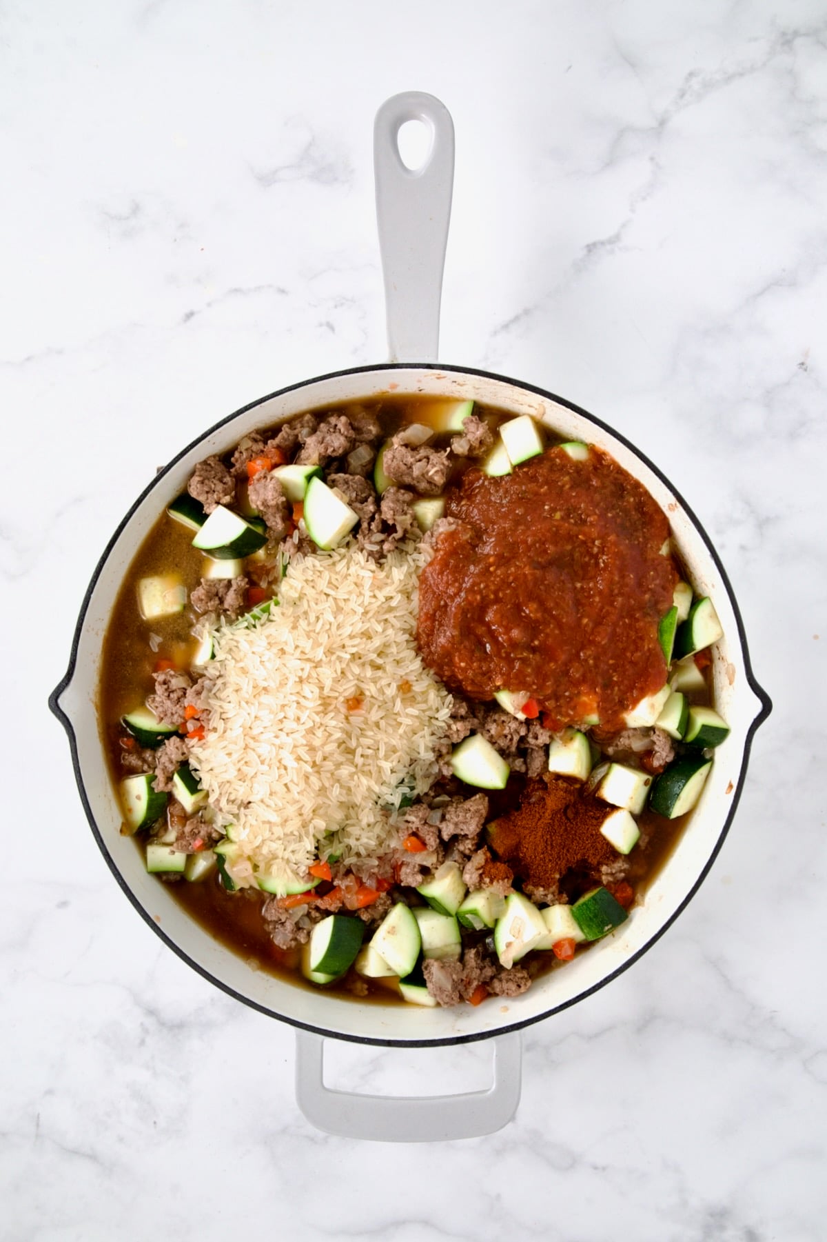 Rice, salsa and spices added to beef and vegetables in white enamel cast iron skillet.
