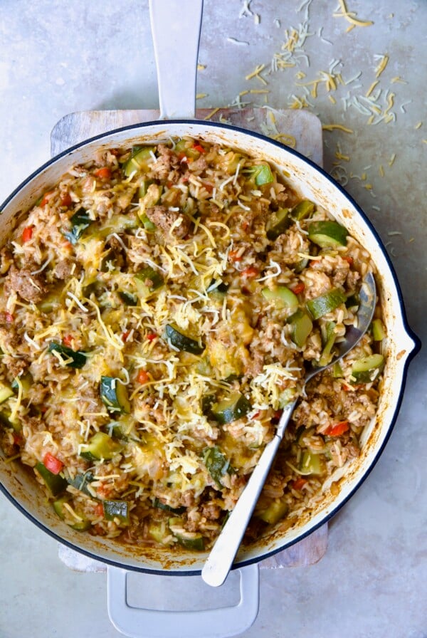 Beef Zucchini Rice Skillet in white enamel cast iron skillet on white piece of wood with serving spoon.