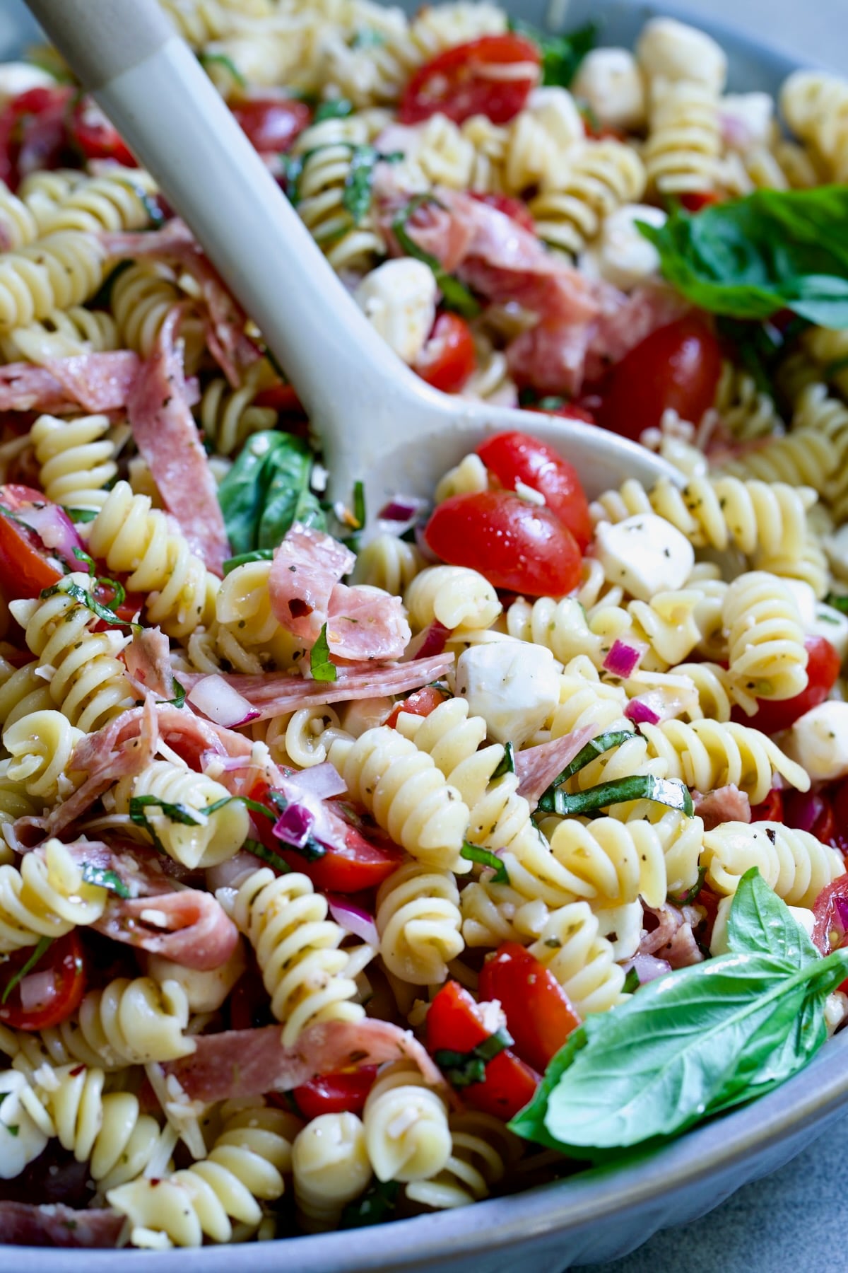 Caprese Pasta Salad in blue bowl being stirred with serving utensil.