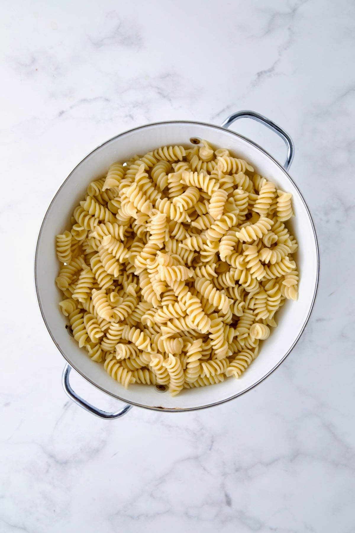 Rotini pasta in white enamel colander.
