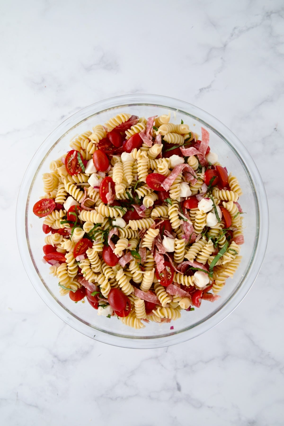 Ingredients for Caprese Pasta Salad in glass bowl after being stirred together.