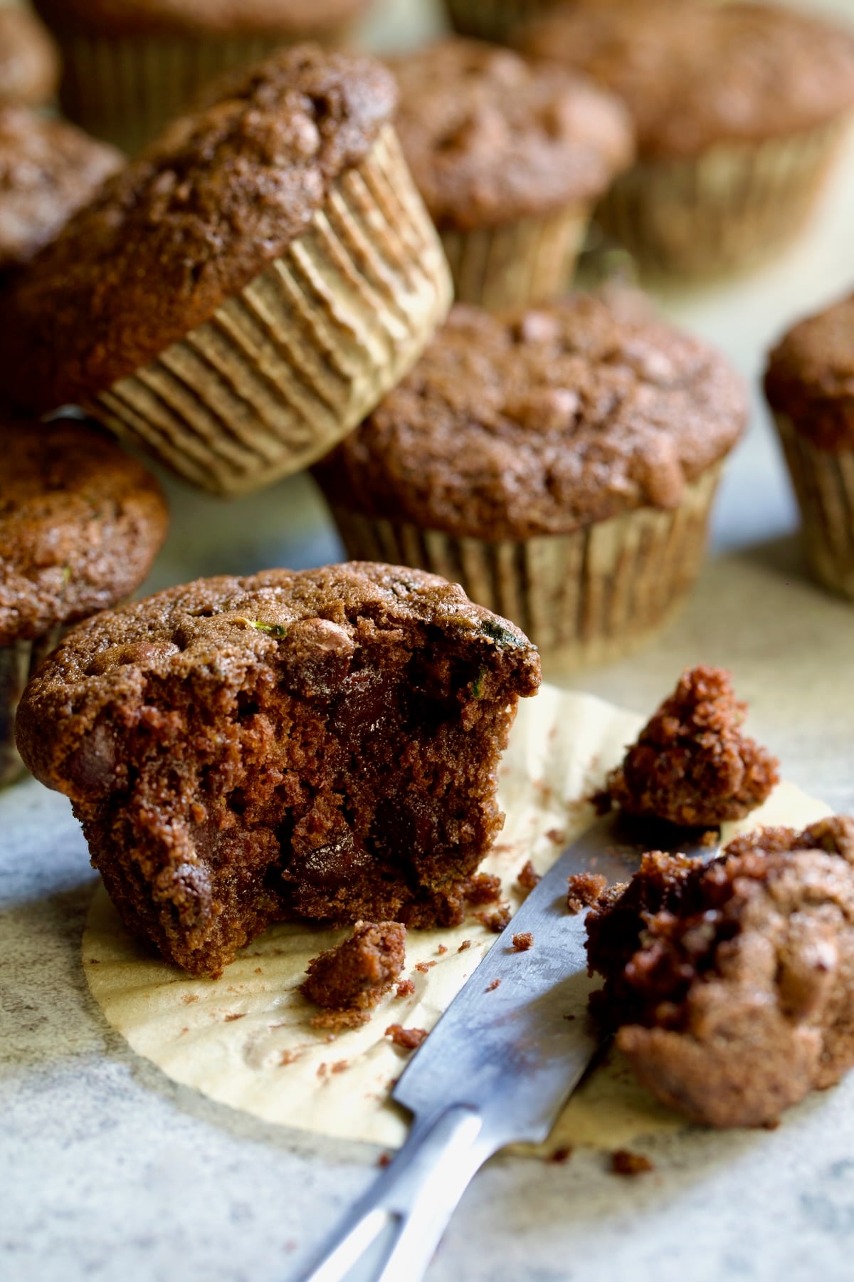 Half a Chocolate and Zucchini Muffin on paper muffin pan liner with table knife.