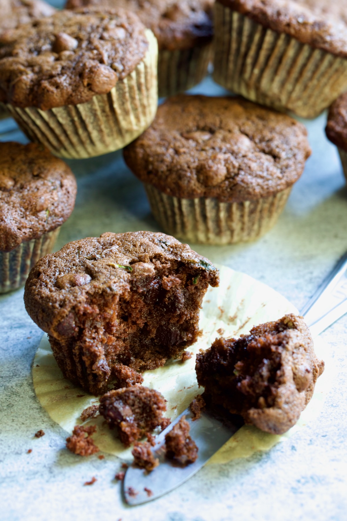 Half a Chocolate and Zucchini Muffin on paper muffin pan liner with table knife.