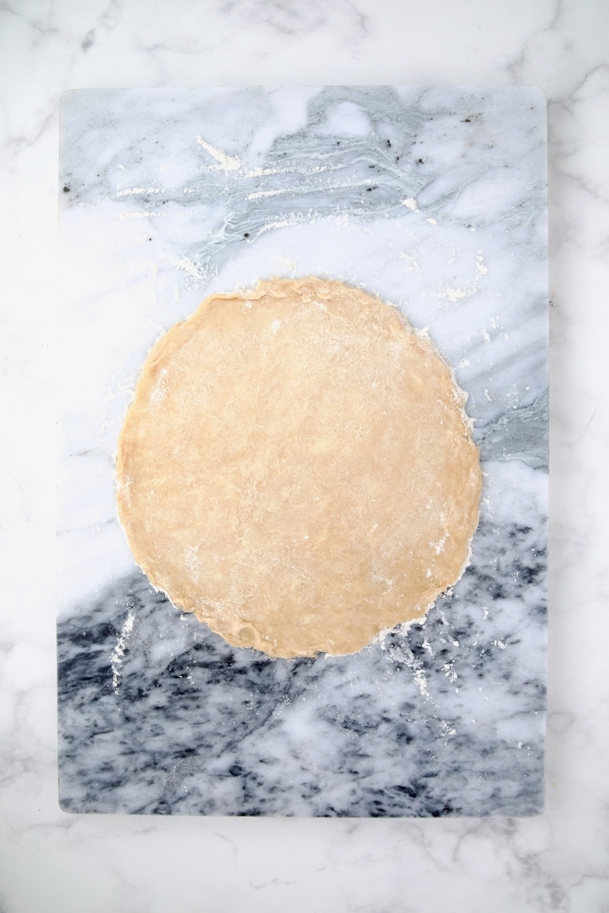 Pie crust dough rolled out onto a marble surface into a circle.