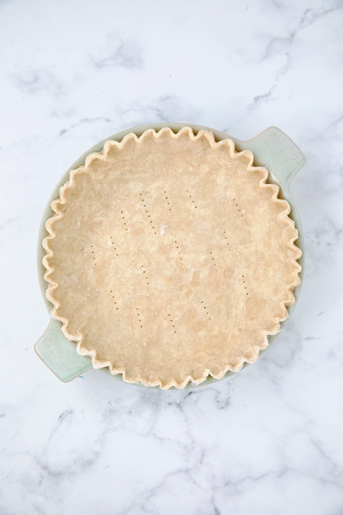 Unbaked pie crust dough docked with a fork in pie pan before being baked.