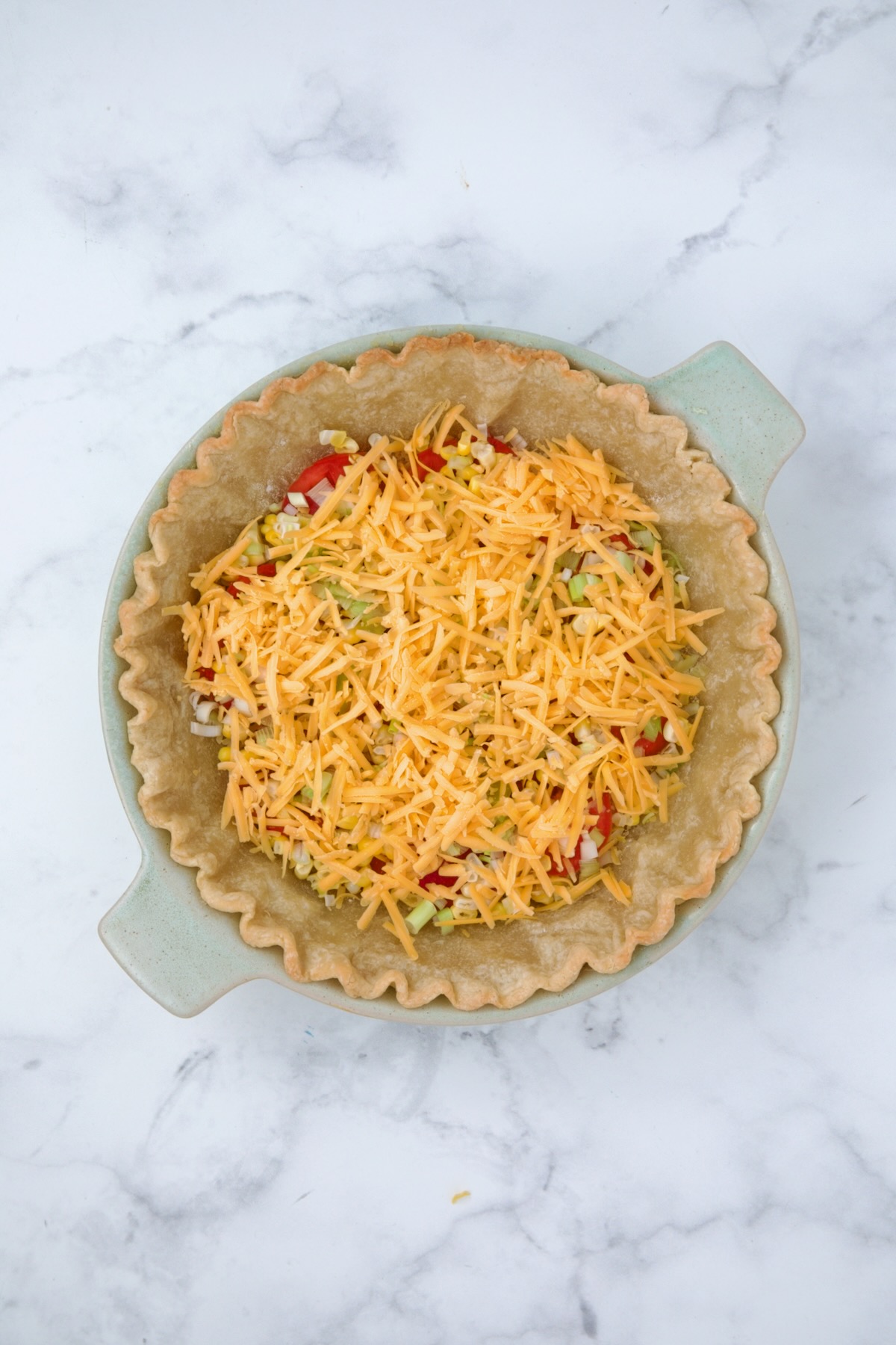 First layer of cheddar cheese sprinkled over tomatoes, corn and scallions.