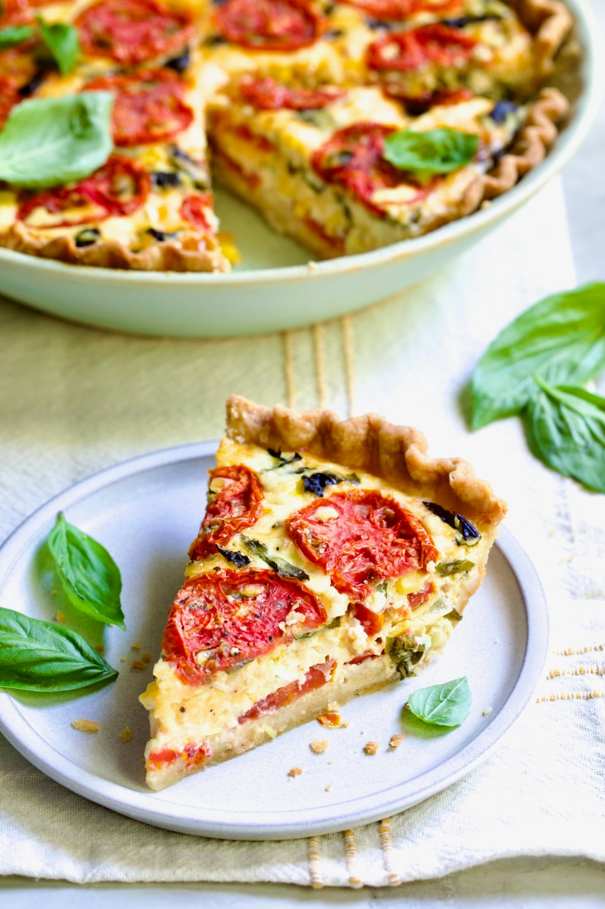 Piece of Tomato Pie Recipe with Corn and Basil on small round plate garnished with fresh basil leaves.