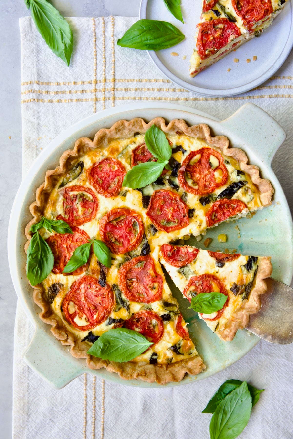 Tomato Pie Recipe with Corn and Basil on yellow striped napkin with two wedges removed garnished with fresh basil.