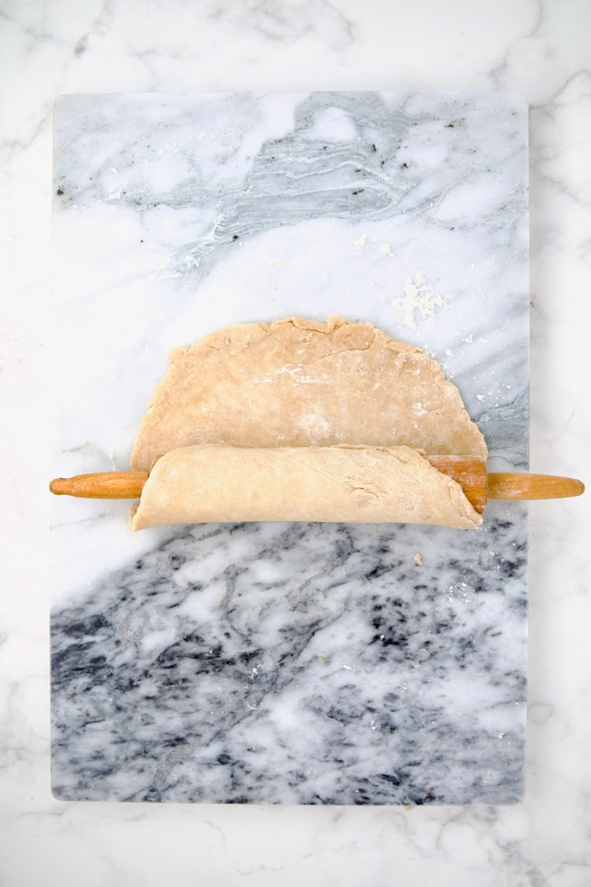 Pie crust dough on marble board with rolling pin.