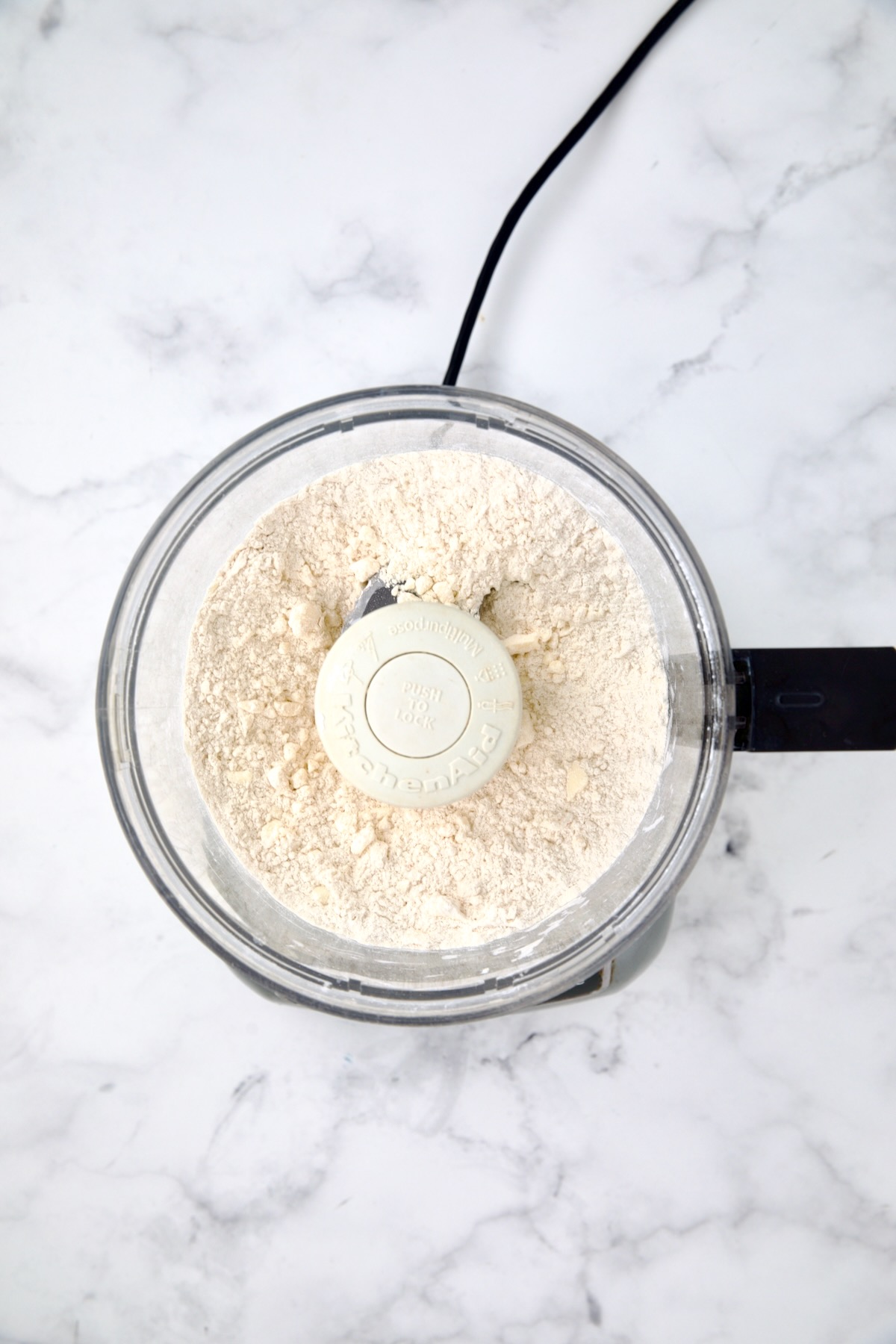 Flour, butter and salt in bowl of food processor after being combined.