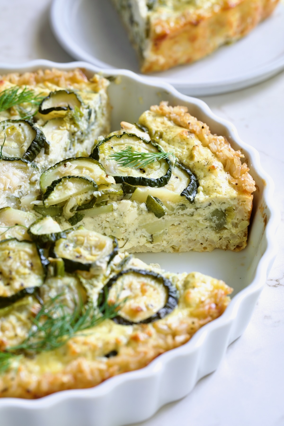Wedge of Zucchini Quiche in white quiche dish.