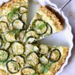 Zucchini Quiche in white quiche dish with pie server picking up a piece.