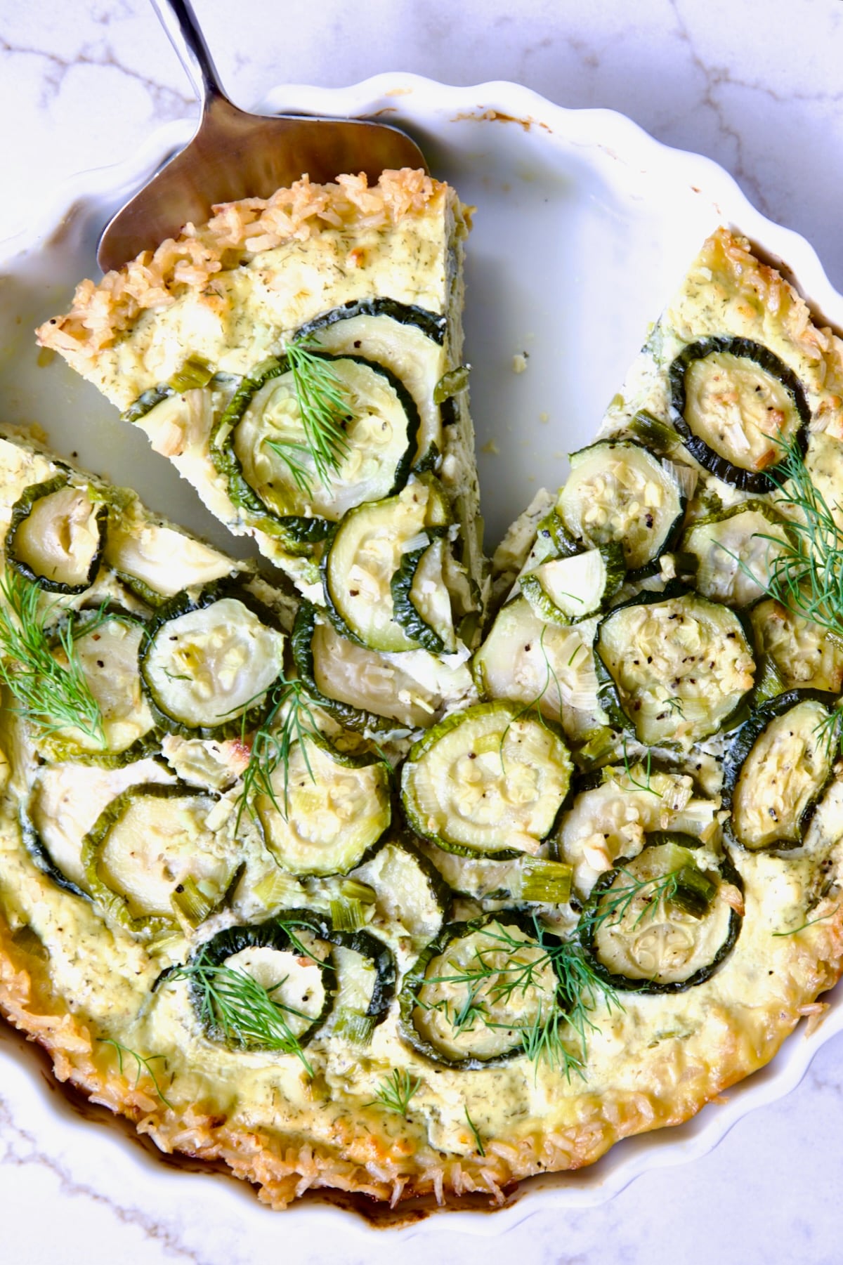 Zucchini Quiche in white quiche dish with pie server picking up a piece.