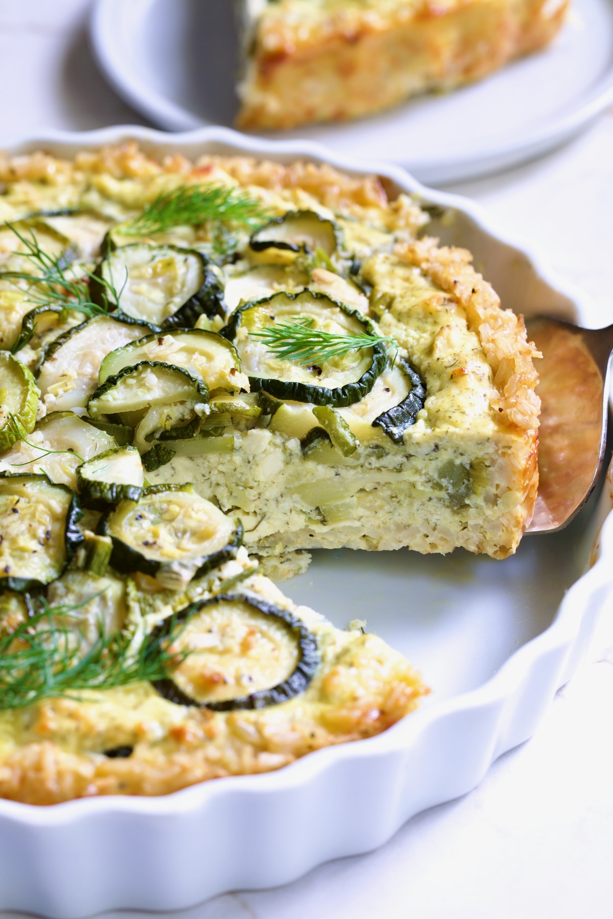 Zucchini Quiche in white quiche dish with pie server picking up a piece.