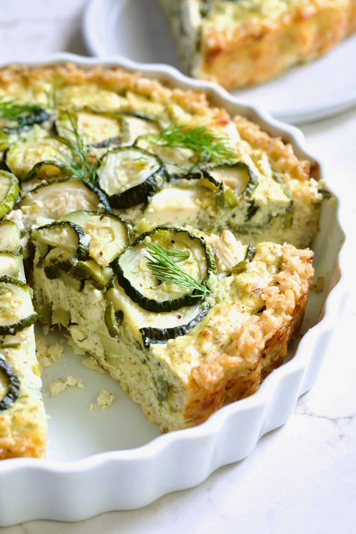 Wedge of Zucchini Quiche in white quiche dish.