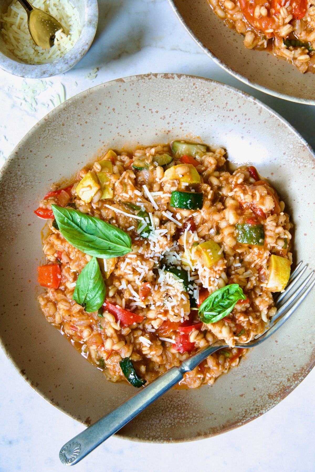 One serving of Barley Vegetable Risotto in brown bowl garnished with fresh basil leaves.