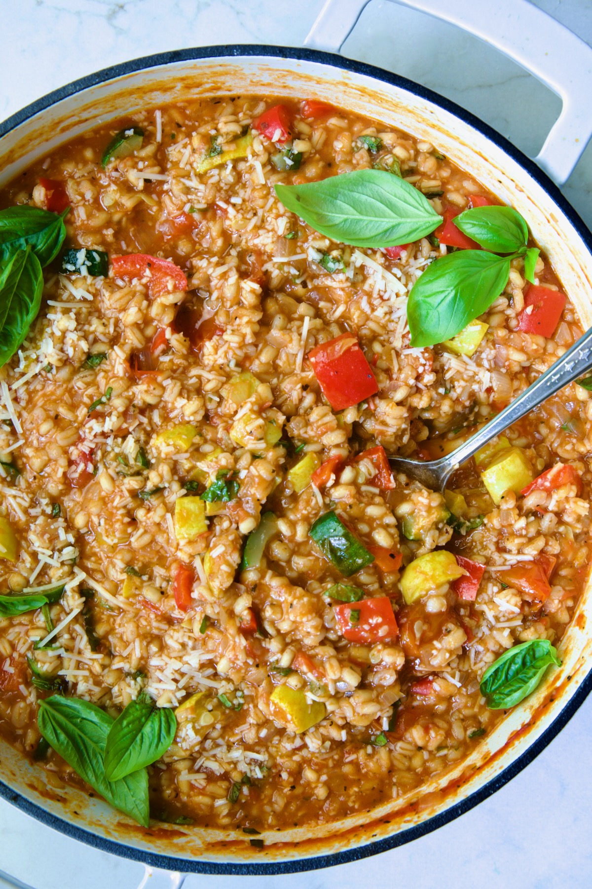 Barley Vegetable Risotto in white enameled cast iron pan garnished with fresh basil.