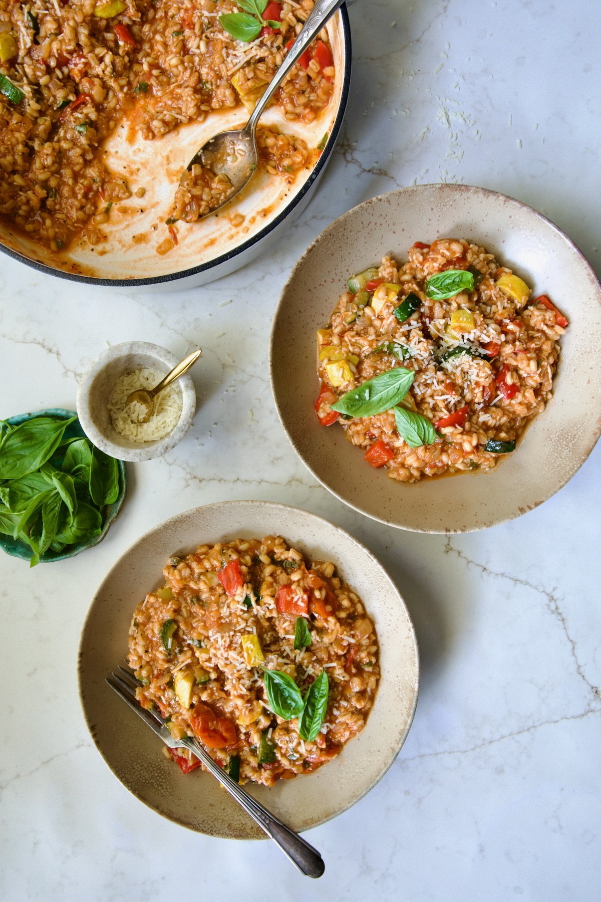 Two servings of Barley Vegetable Risotto in brown bowls garnished with fresh basil.