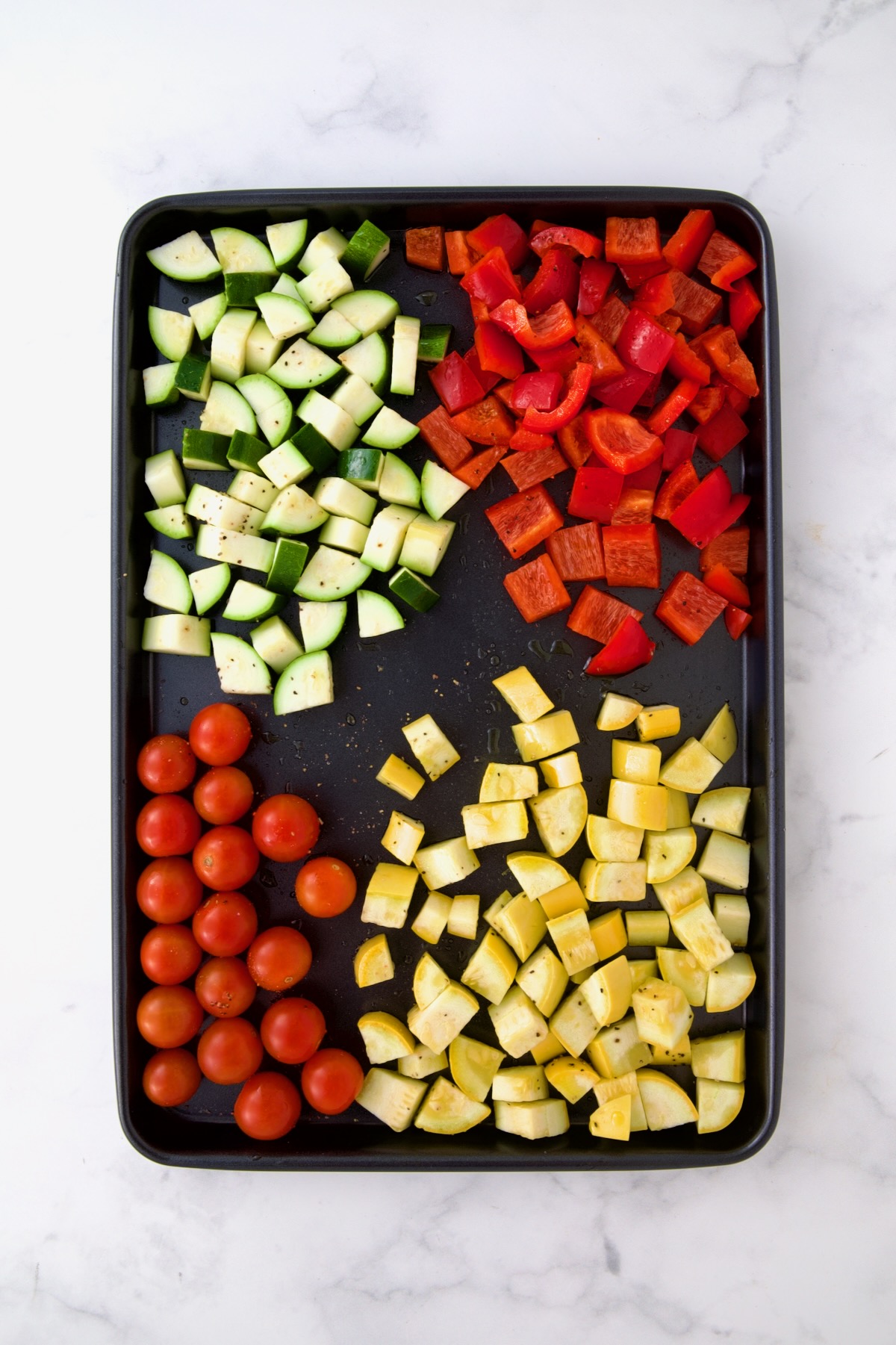 Zucchini, red bell pepper, yellow squash and cherry tomatoes on rimmed baking sheet before being roasted.
