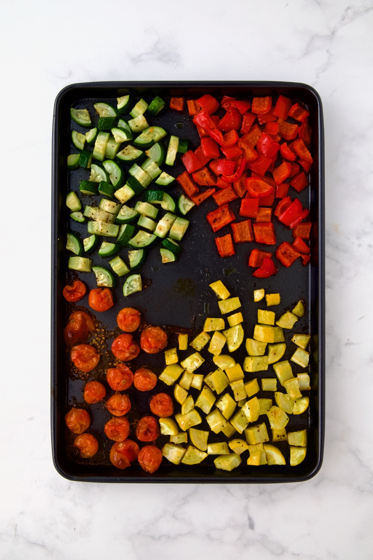 Zucchini, red bell pepper, yellow squash and cherry tomatoes on rimmed baking sheet after being roasted.