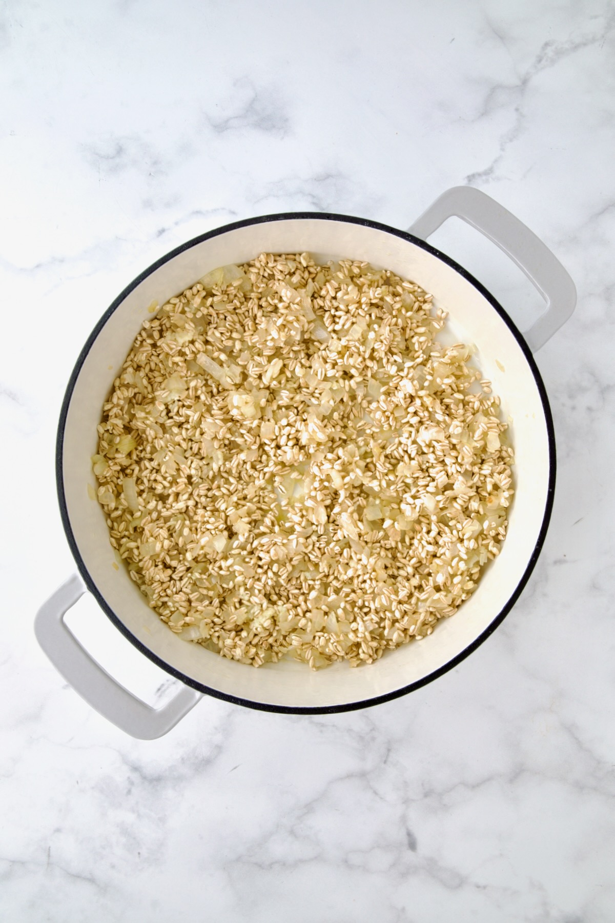 Cooked chopped onions, garlic and uncooked barley in white enamel cast iron skillet.