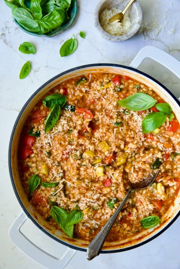 Barley Vegetable Risotto in white enameled cast iron pan garnished with fresh basil.