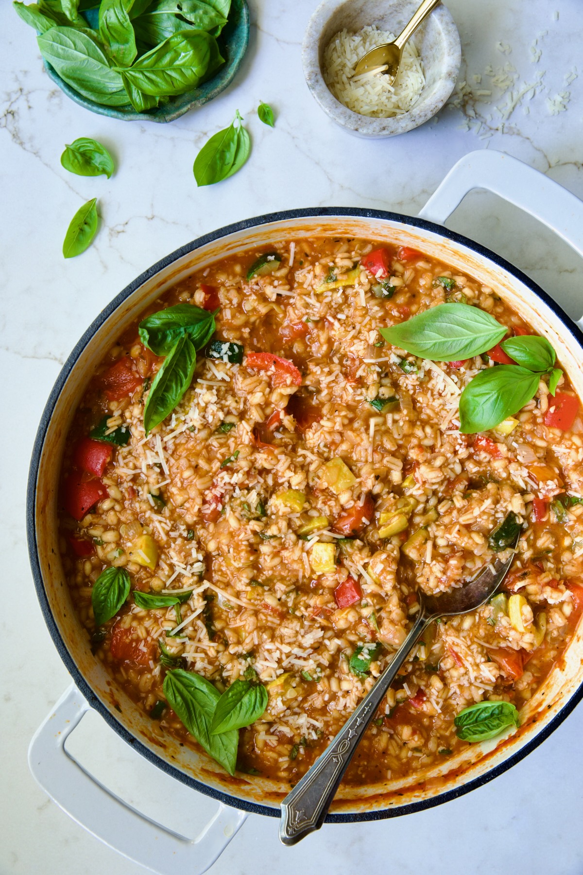 Barley Vegetable Risotto in white enameled cast iron pan garnished with fresh basil.
