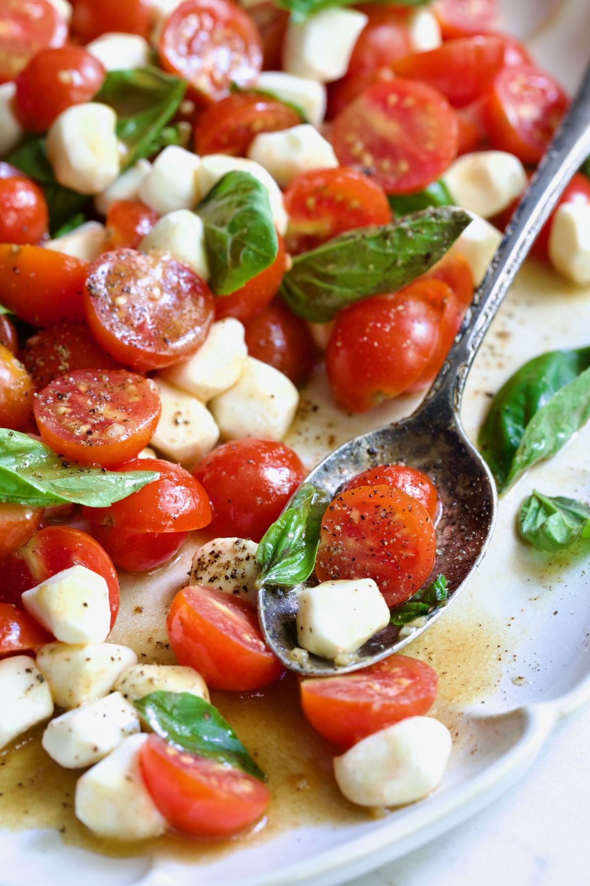 Caprese Salad with Cherry Tomatoes on white oval platter with serving spoon.